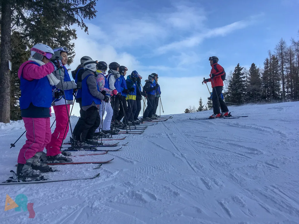 Skigruppe steht in einer Reihe am Pistenrand.